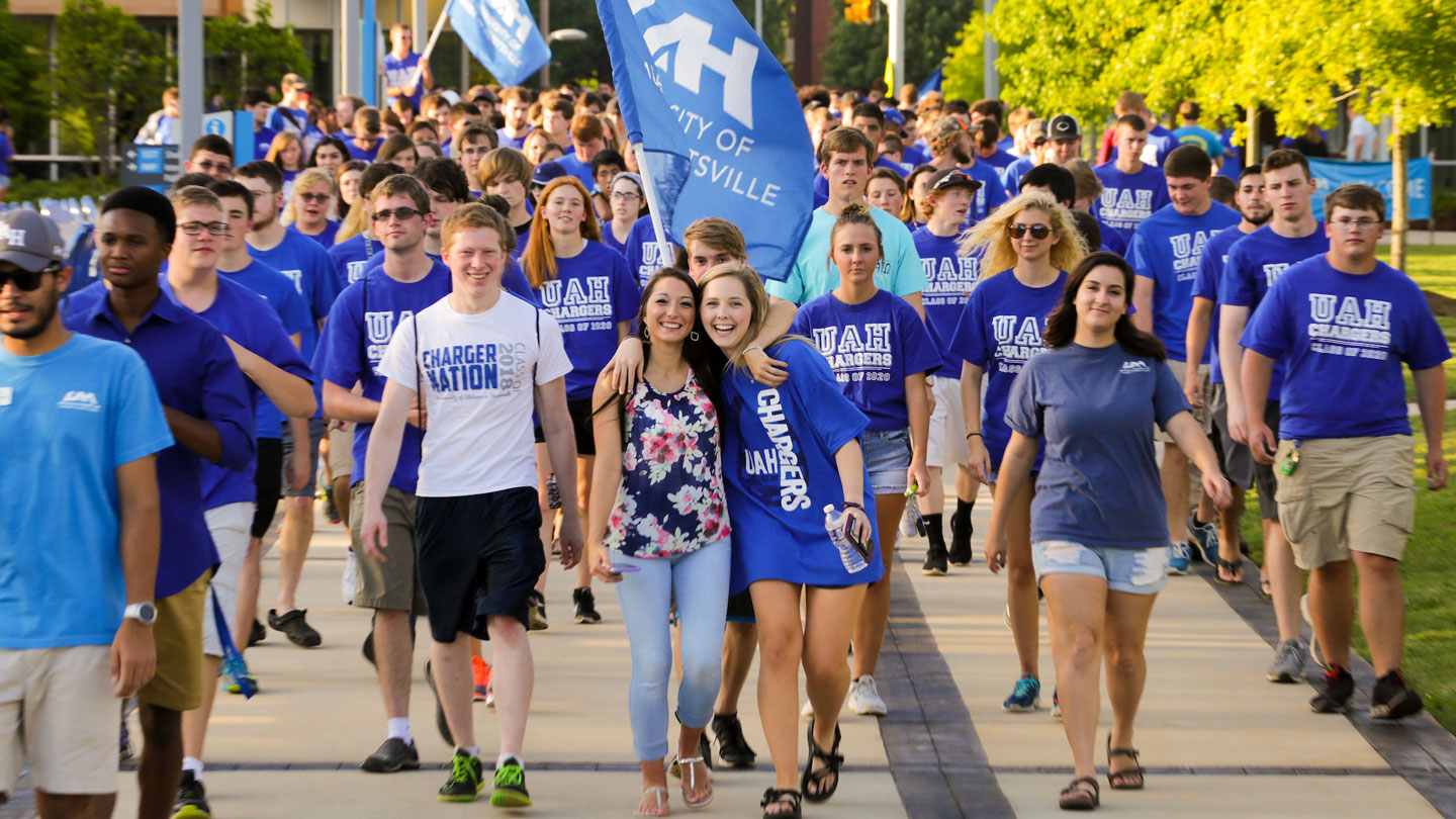 A crowd of smiling U A H students march down the campus greenway during the convocation ceremony.