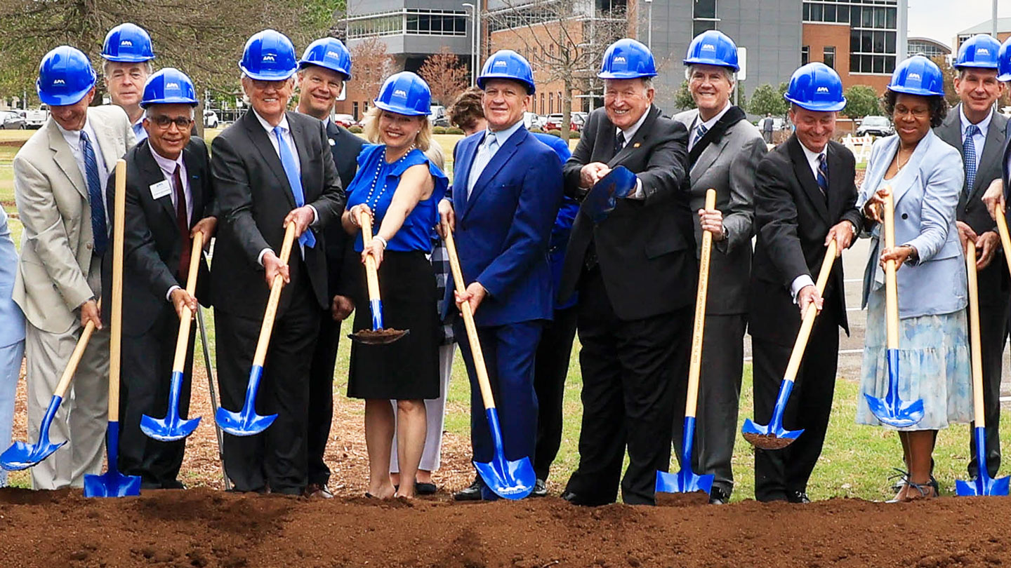 A group of UAH and community leaders wearing blue hardhats break ground on a new construction project on the UAH campus.