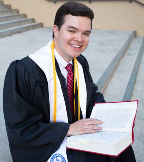 Bobby Marsh wearing graduation attire setting on steps.