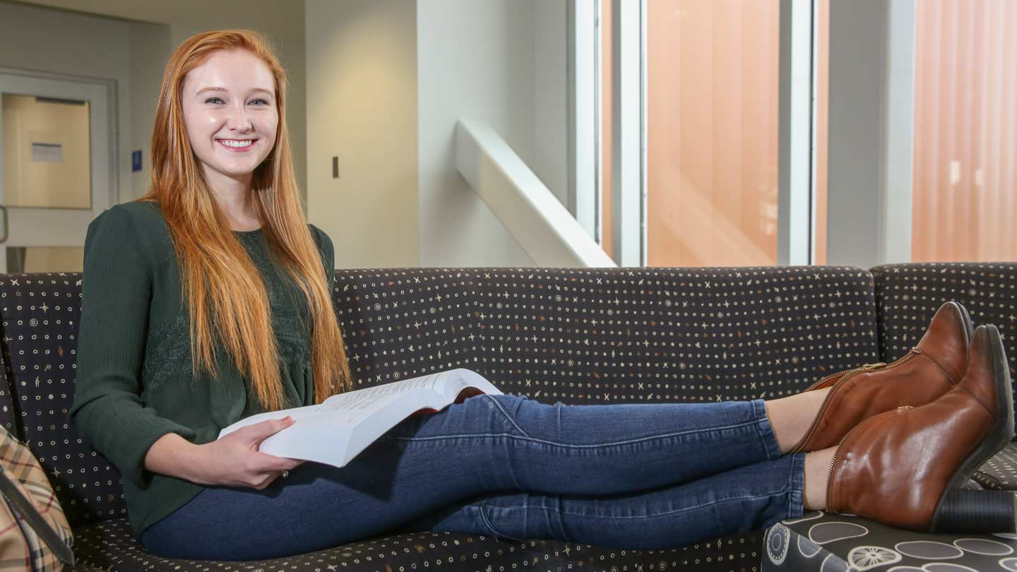UAH Student Molly Ford smiling and reclining on a sofa