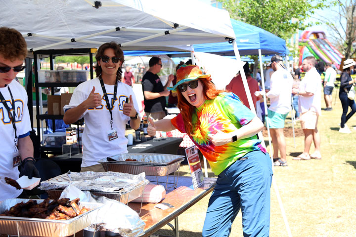 A vibrant outdoor festival scene showcasing food stalls, colorful tents, and attendees enjoying various activities in a sunny park setting.