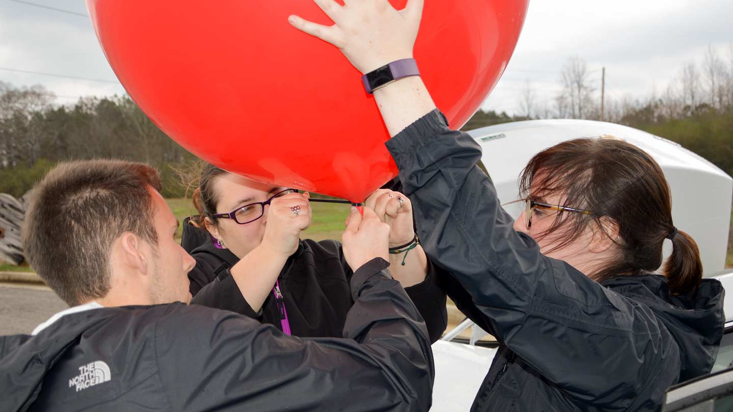 Three UAH undergraduate students attaching an instrument payload to a weather balloon