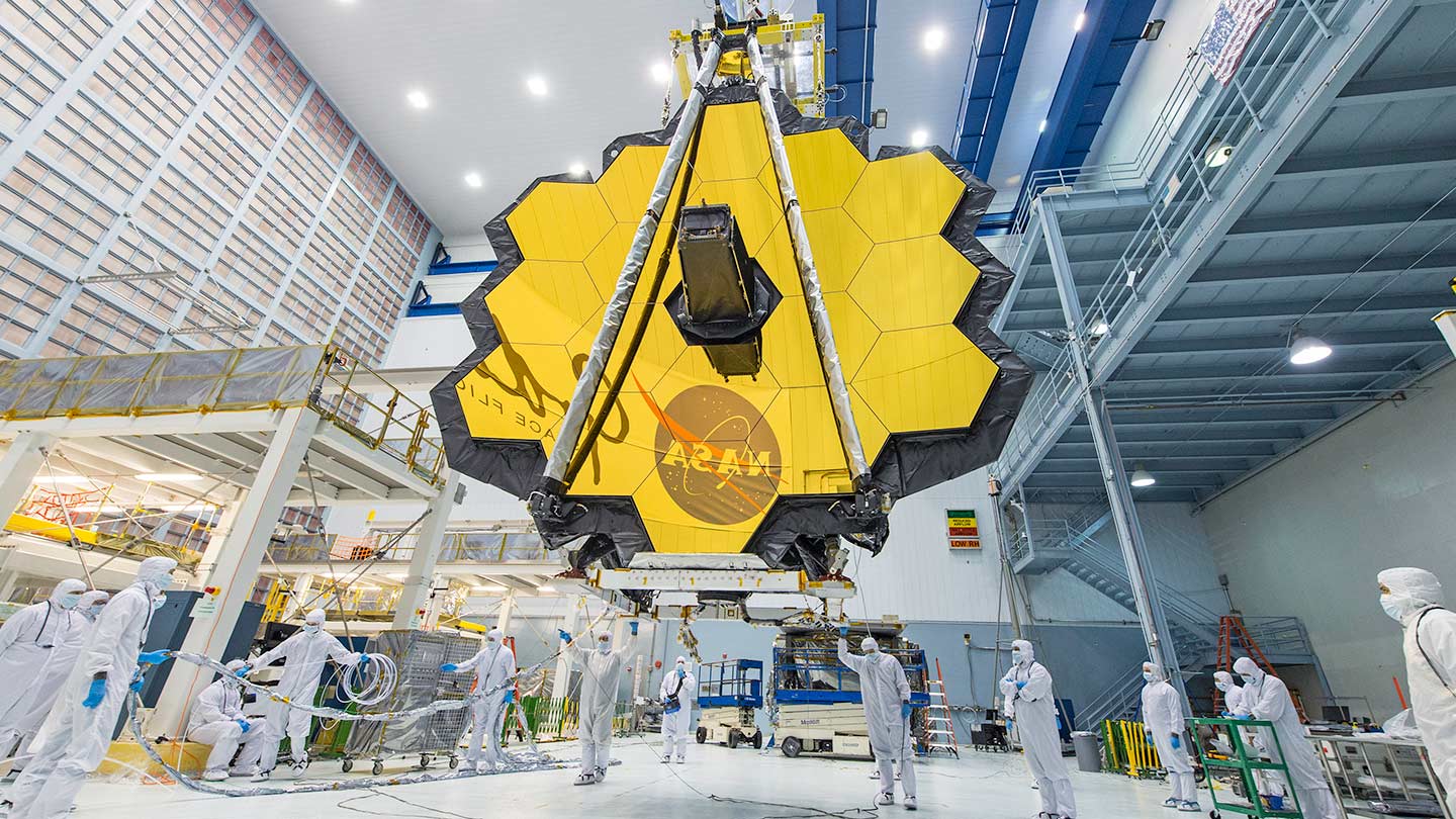 Fully deployed James Webb Space Telescope being moved by crane.