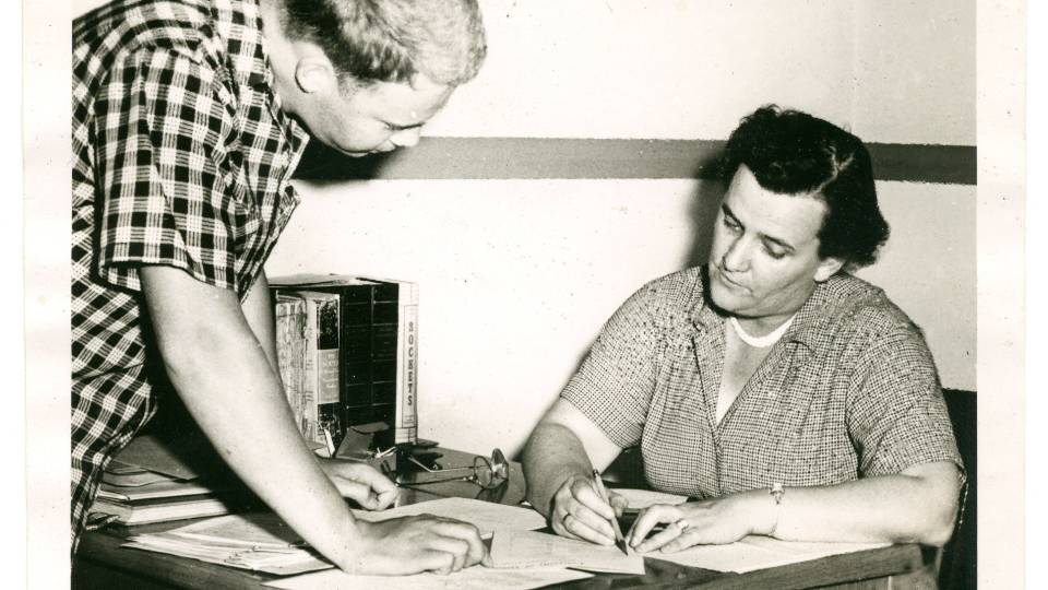 Dr. Roberts seated at a desk with a student looking over