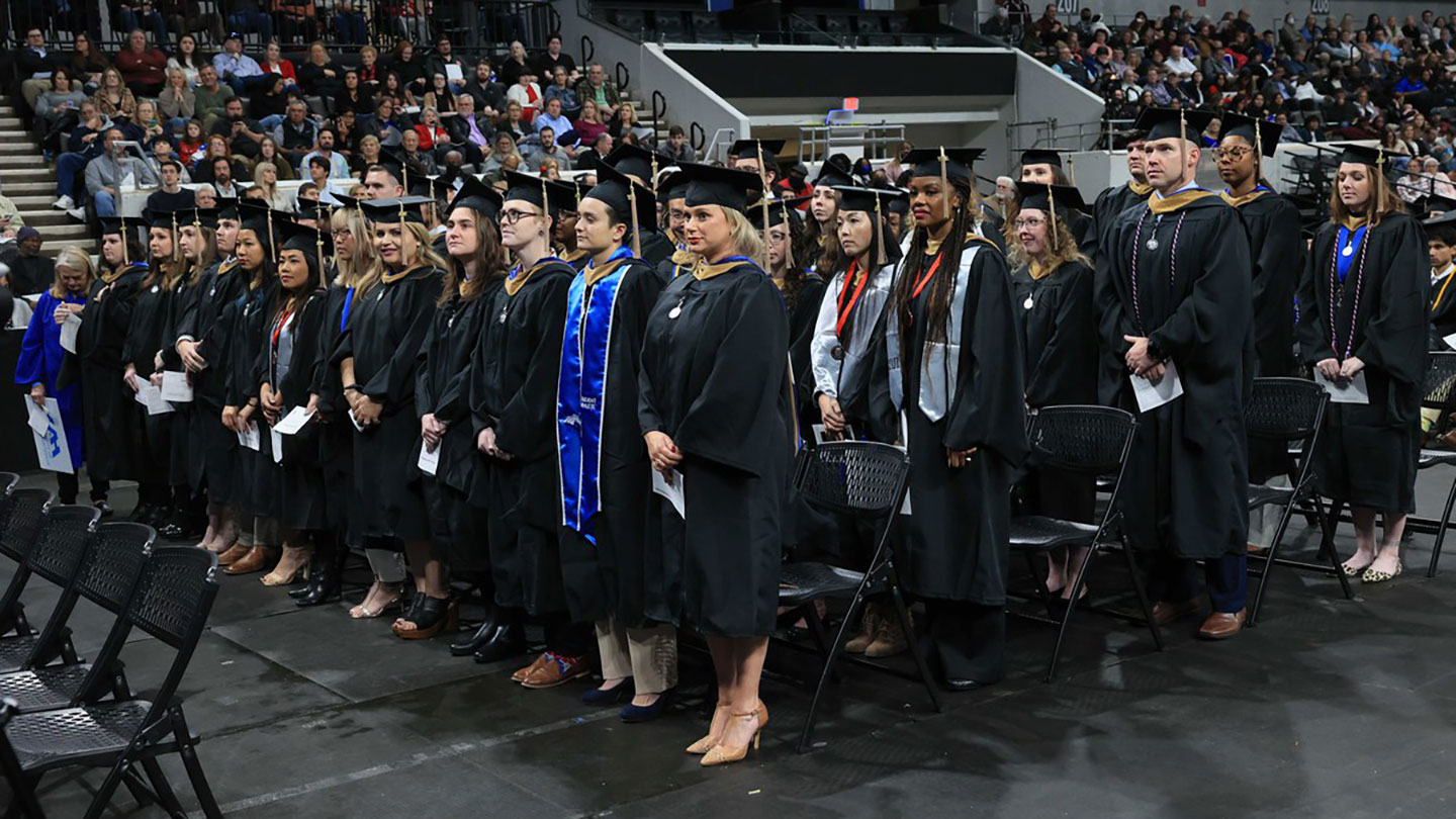 many graduates in caps and gowns standing in rows