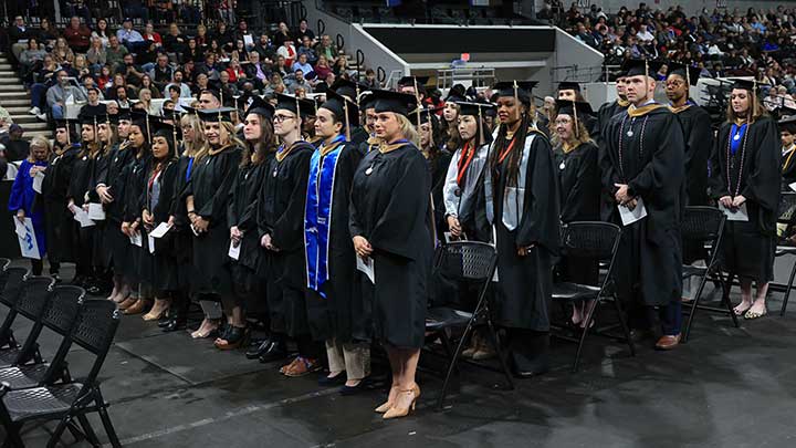 many graduates in caps and gowns standing in rows ?>