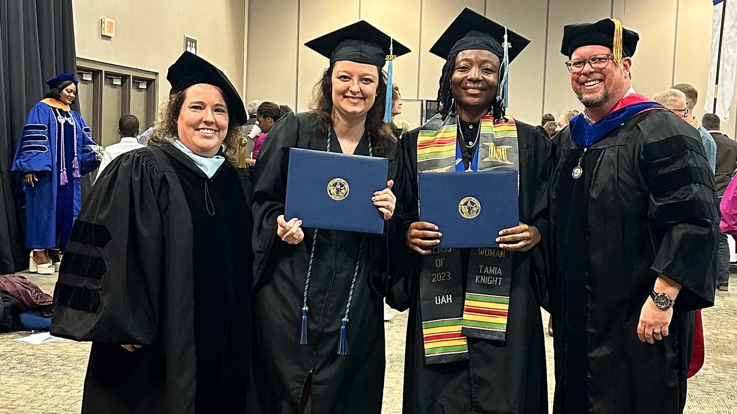 four people in graduation gowns posing for photo.