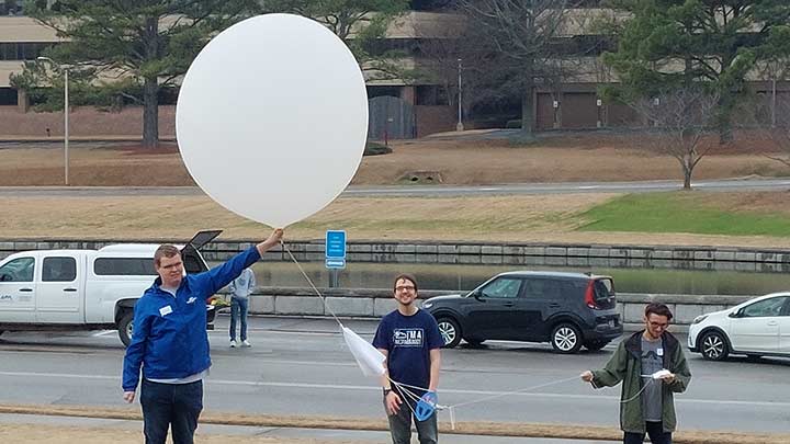 Three students standing outside holding a weather balloon.
