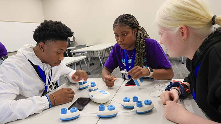 Students setting around a table working together with cybersecurity devices.