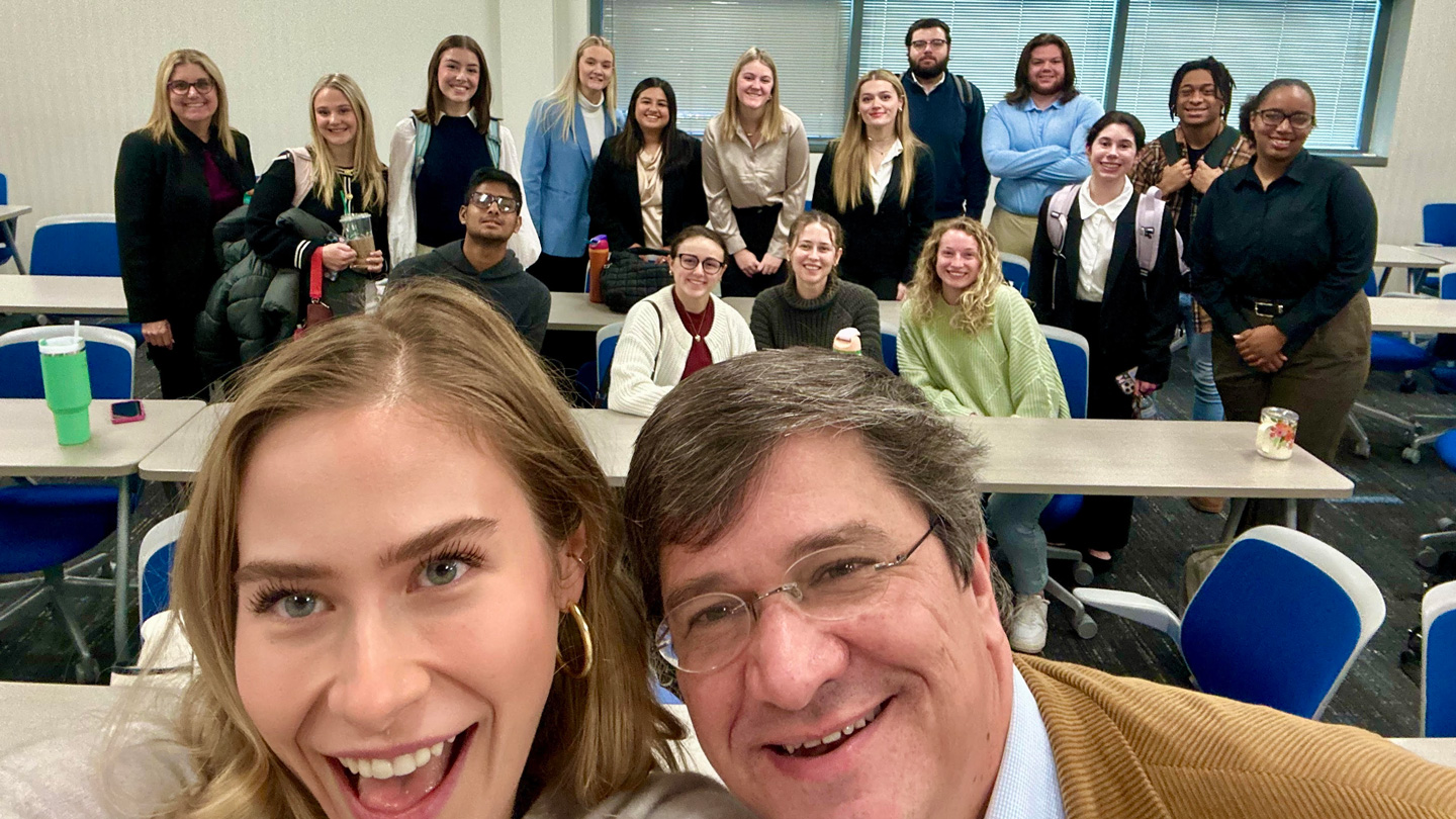 Group of people standing and sitting in a classroom setting.