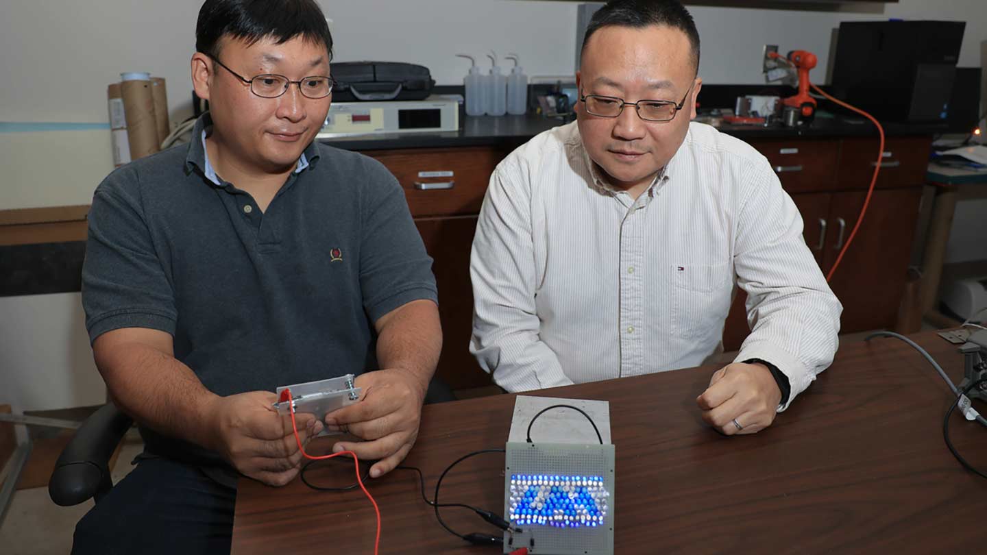 Dr. Moonhyung Jang and Dr. Gang Wang in a lab setting working with electronics on a table.