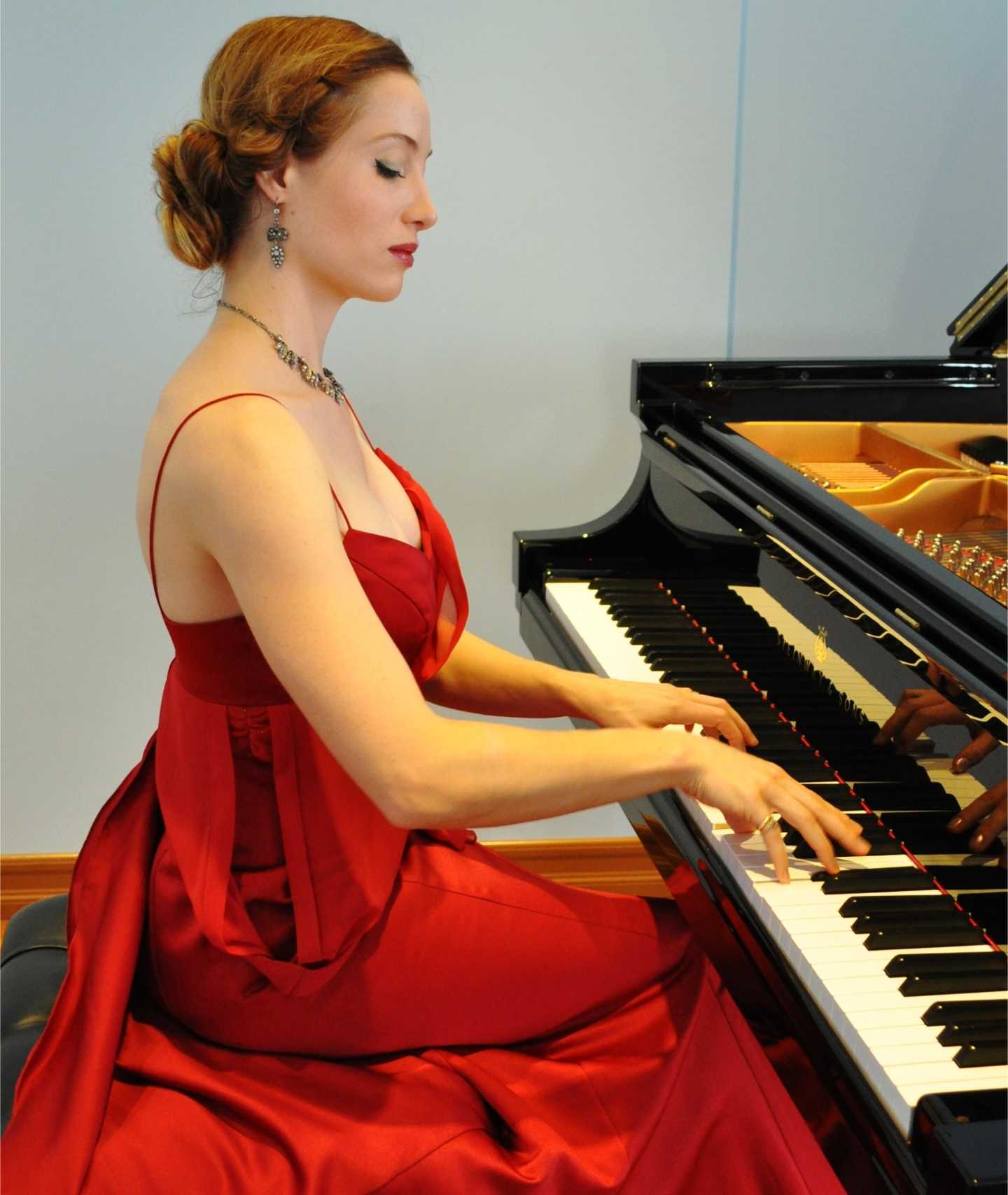 Photo of Danae Xanthe Vlasse performing in a red dress at a piano.