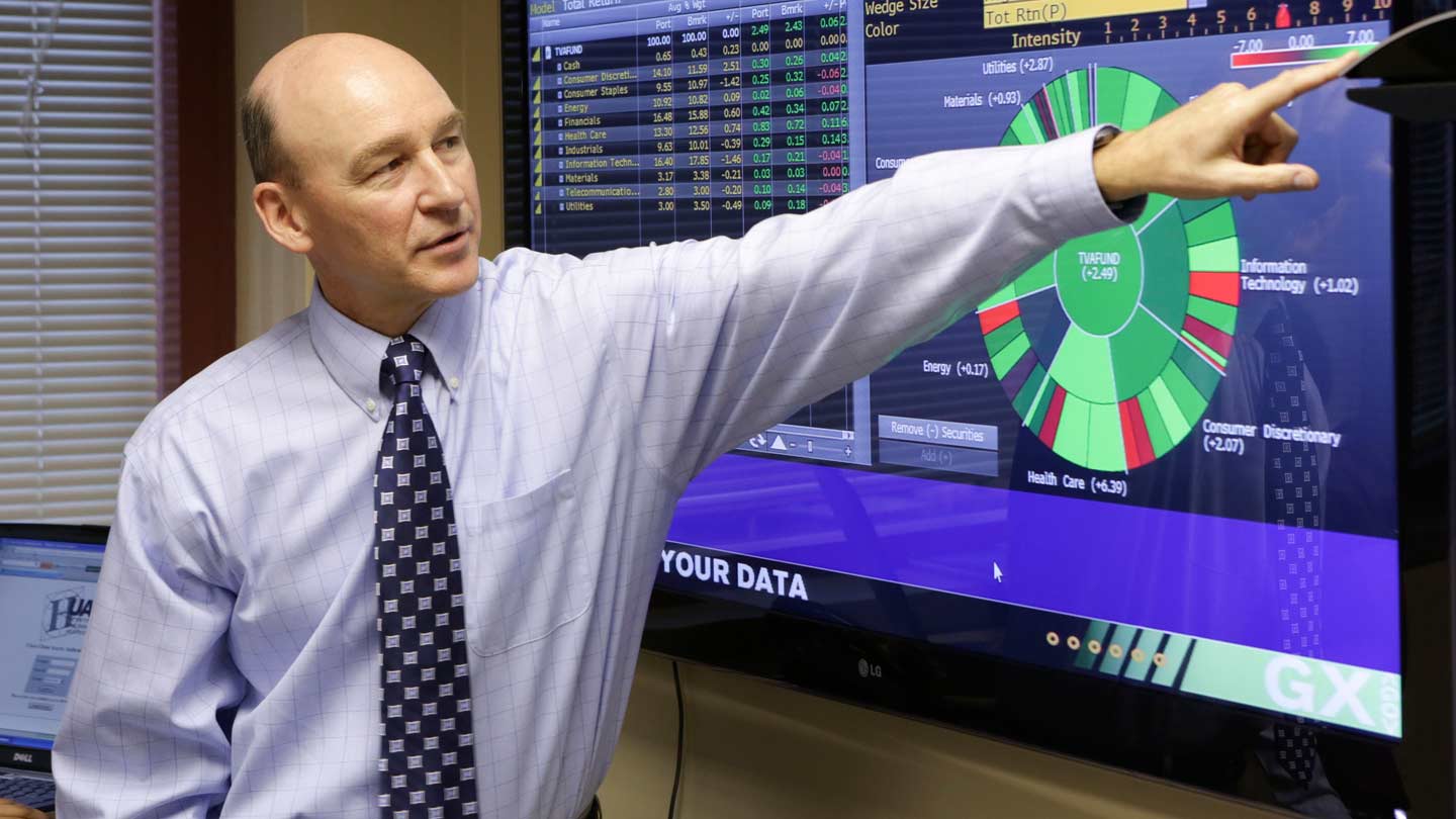 John Burnett pointing at monitor displaying statistics.