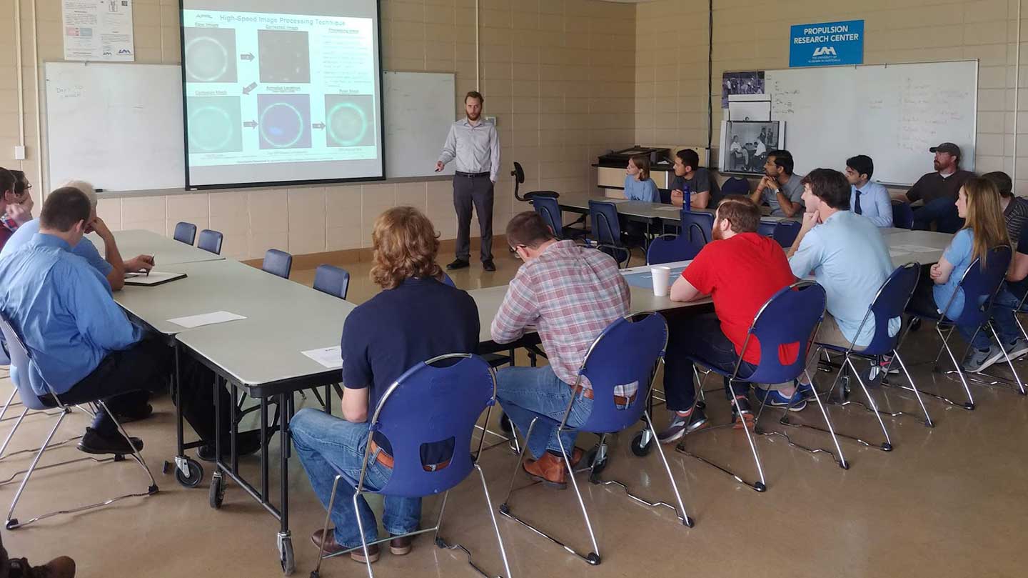 Blaine Bigler presenting in front of an audience setting around a table.