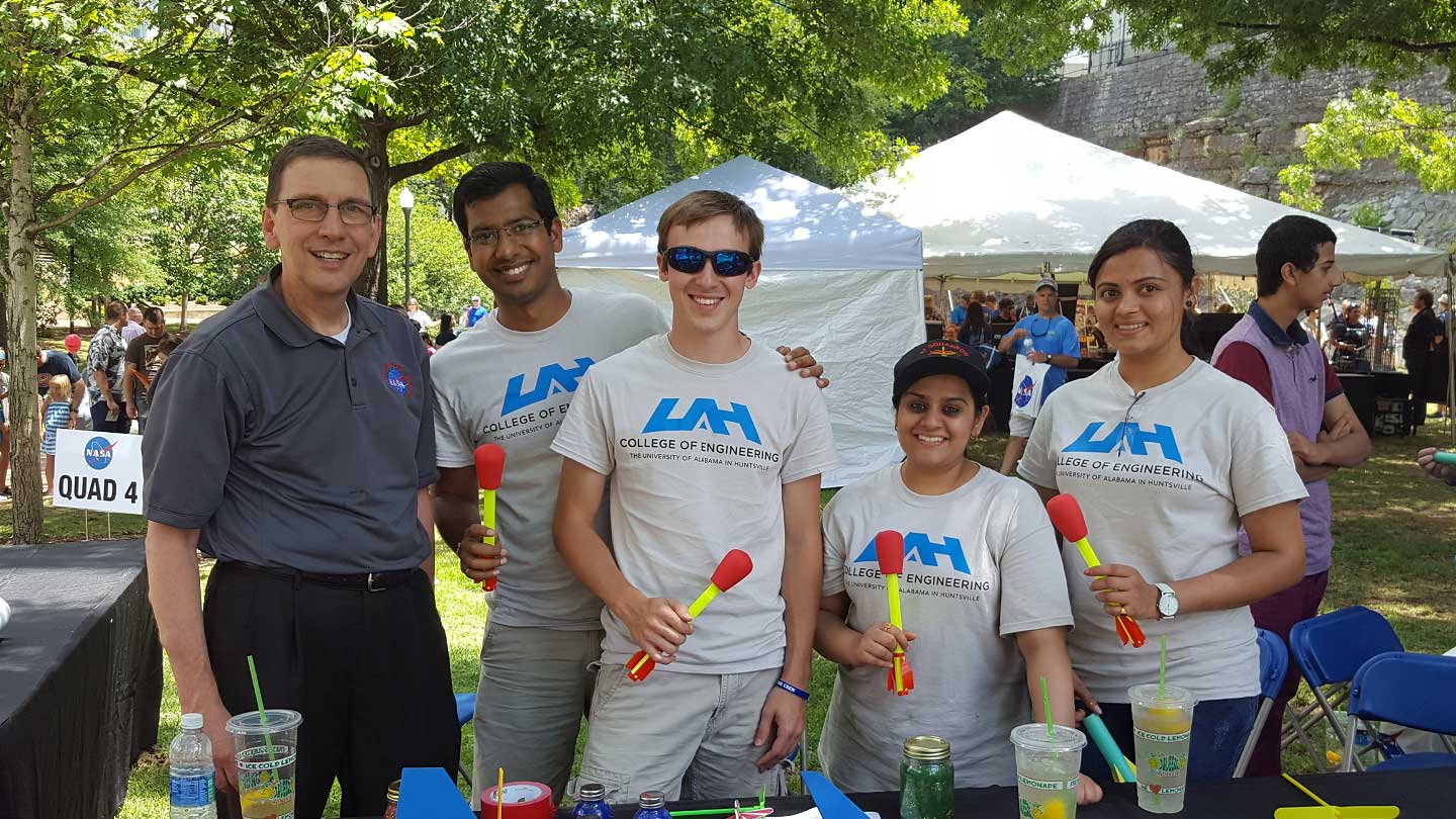 four engineering students holding model rockets pose with a nasa representative