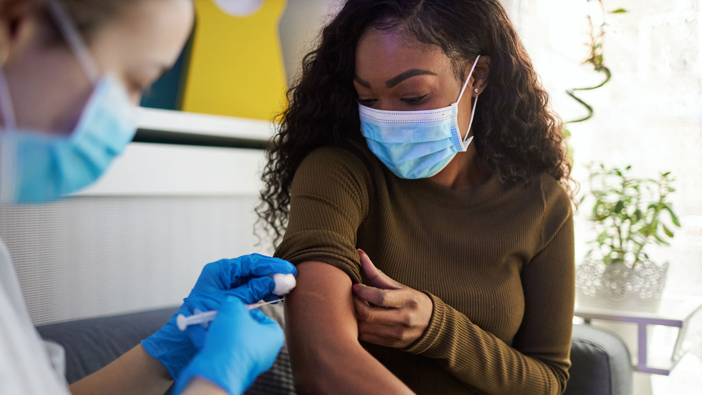 young woman of color receiving a vaccine from medical professional