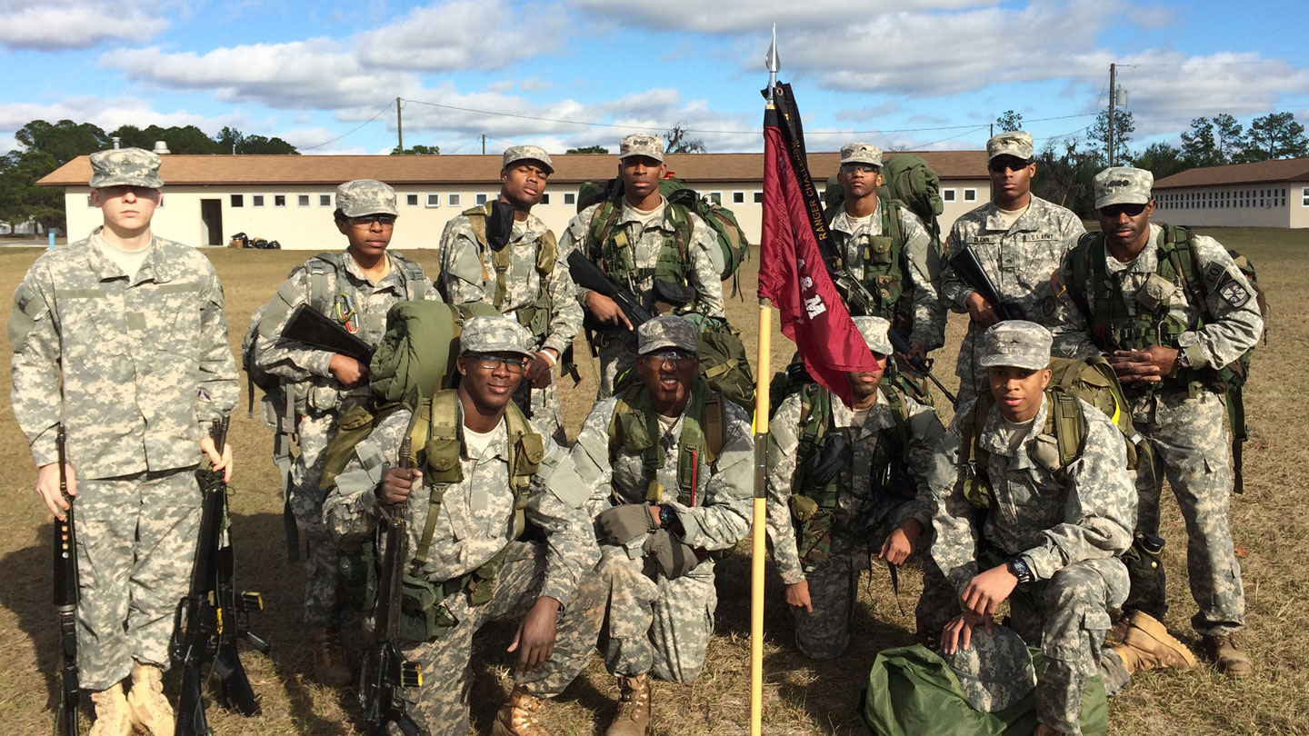 men and women in uniform kneel by a flag